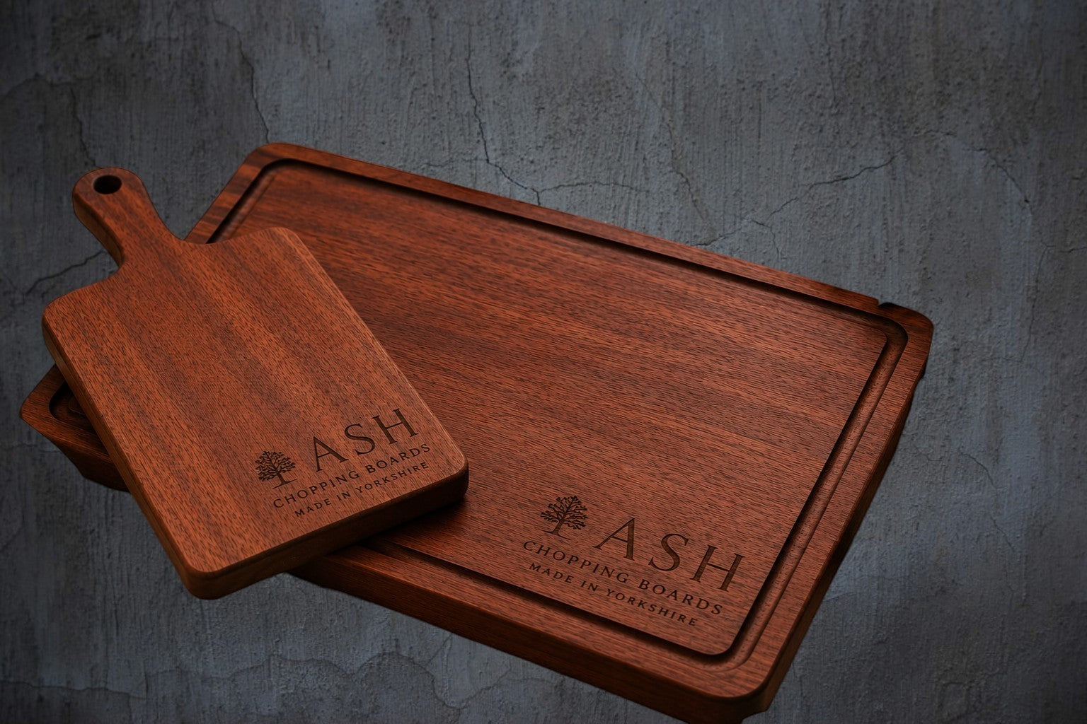 ASH Chopping Boards personalised wooden chopping and cheese board set with engraved logo on a dark textured background