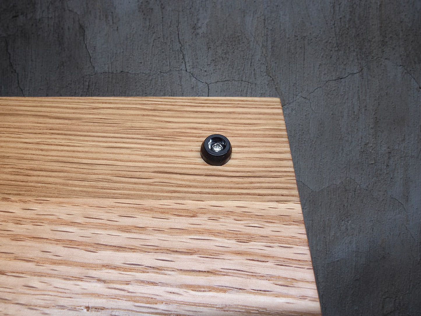 A small black circular accessory with a clear center sits on a wood-grain surface next to a blue cutting mat with grid lines.