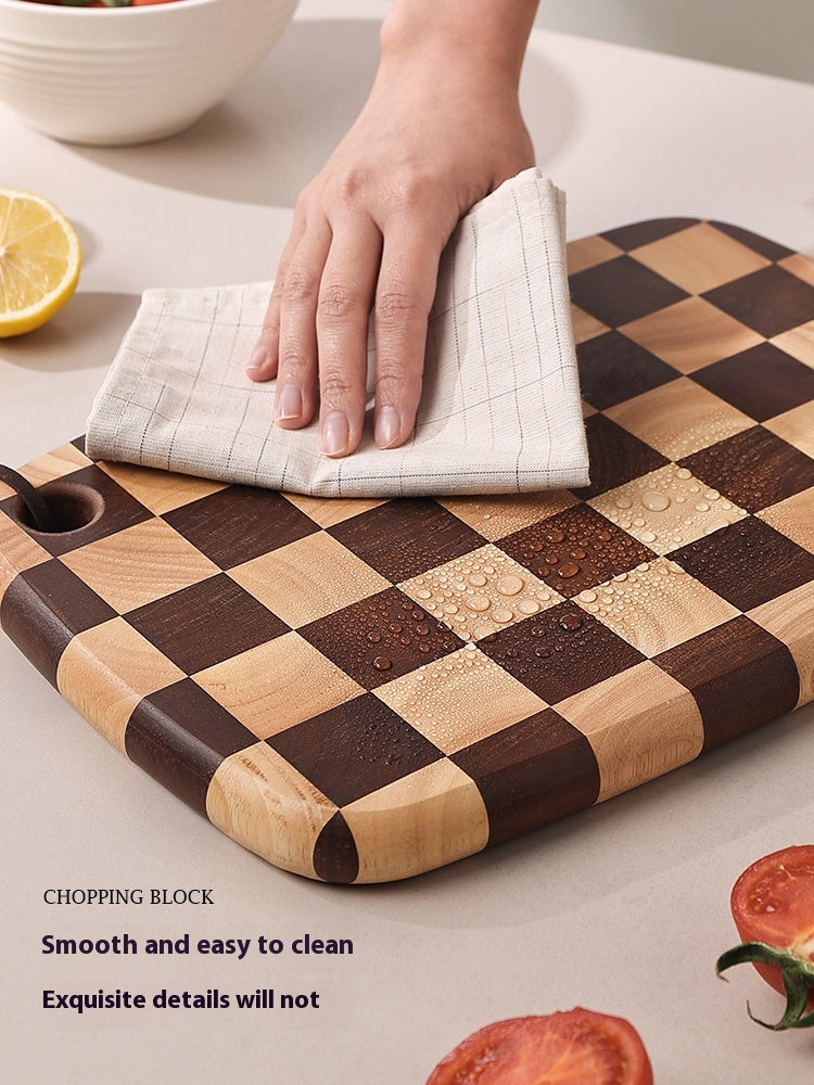 Wooden checkered cutting board with a hand using a cloth to clean it, surrounded by kitchen items.